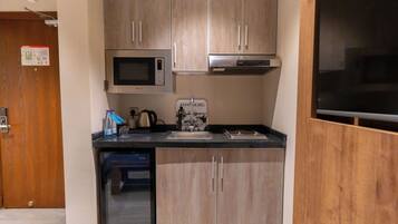 Una cocina compacta con armarios de madera, un microondas, una cafetera y un lavabo.