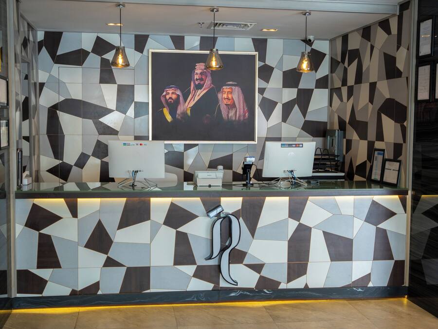 A reception desk with a geometric patterned wall, two monitors, and a pendant light.