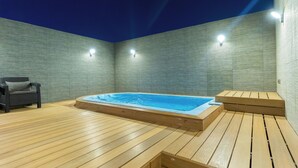 A wooden deck with a hot tub and a chair, surrounded by walls with built-in lighting. - RASIA HOTEL  (Jeddah)