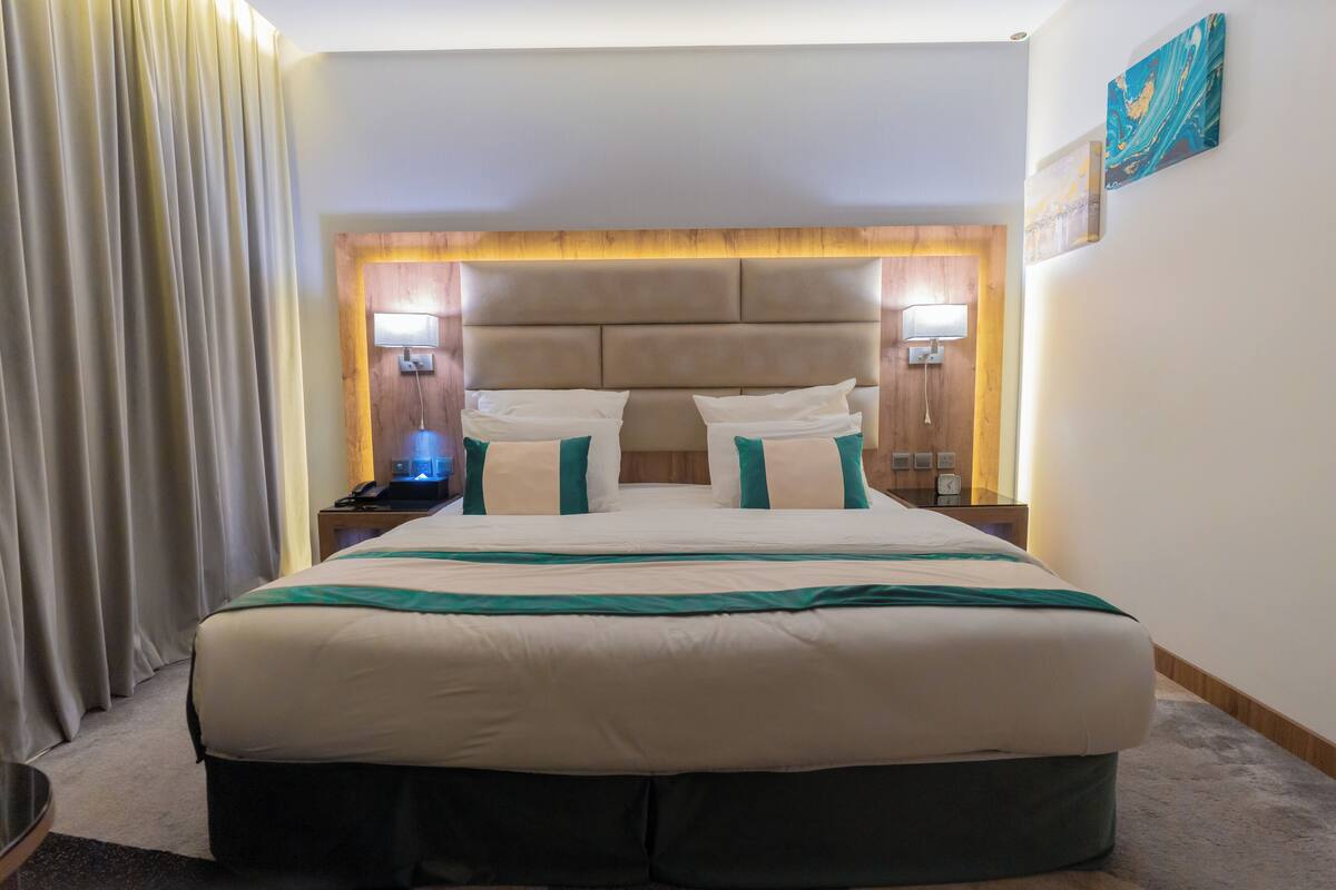 Quarto de hotel com cama grande, duas mesas de cabeceira e cabeceira com iluminação integrada.