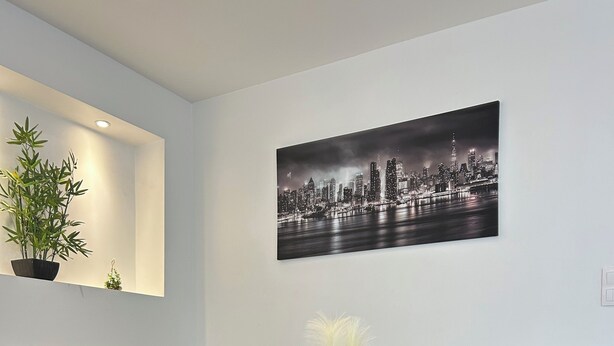 Una sala moderna con una mesa de centro de vidrio, sofá gris y una pintura de un paisaje urbano.