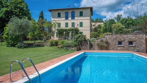 A swimming pool with a stone wall and metal railings, surrounded by a well-maintained lawn and a two-story building with green shutters. - Il Villino Del Collezionista With Pool In Pistoia (Pistoia)