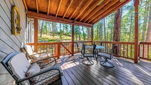Una terraza de madera con mobiliario exterior, vistas a un bosque y el interior rústico de una cabaña.