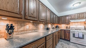 Una cocina con armarios de madera, encimeras de granito, estufa y cafetera.