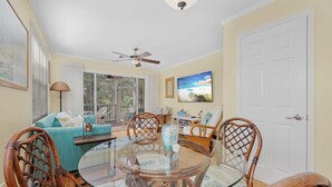 Un coin repas avec une table en verre entourée de chaises en osier, d’un canapé bleu et d’un ventilateur de plafond.