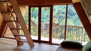 Camera mansarda in legno con una scala in legno, un letto e vista su una lussureggiante foresta.