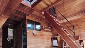 Un interno in legno con una scala che conduce a un livello superiore, un letto con biancheria verde e un piccolo tavolo con una sedia.