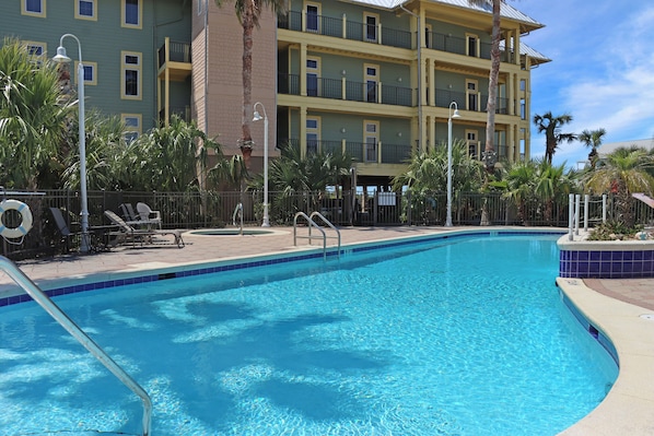 Una piscina con agua cristalina azul, rodeada por una valla, y un edificio con balcones al fondo.