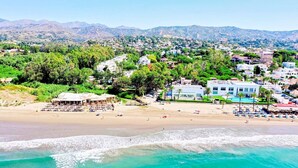 Uma cidade costeira com praia, área de piscina e edifícios com estilo arquitetônico mediterrâneo.