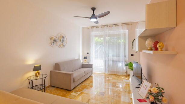 A living room with a sofa, a small table with a lamp, a ceiling fan, and a television. - La Pineta sul Mare by Wonderful Italy (Sanremo)