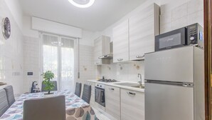 A modern kitchen with white cabinetry, a built-in oven, a microwave, and a refrigerator. There is a dining table with chairs and a potted plant. - La Pineta sul Mare by Wonderful Italy (Sanremo)