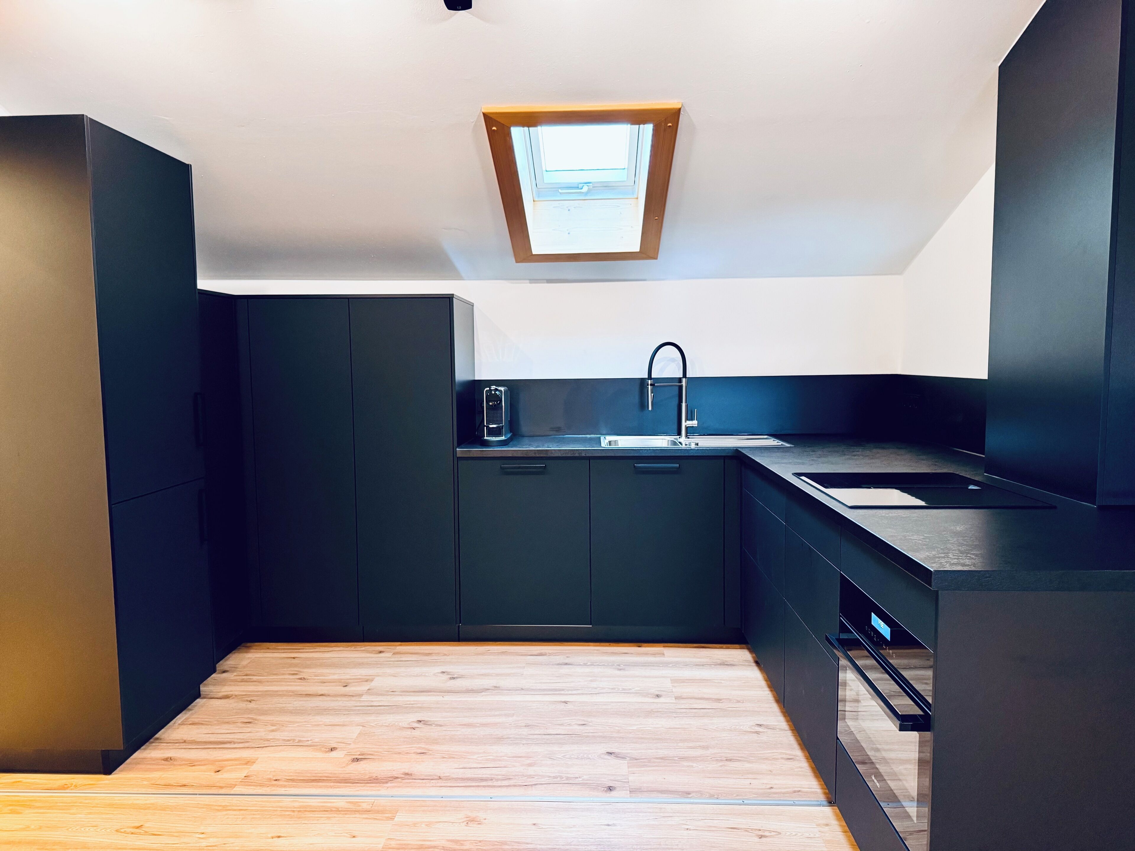 A compact kitchen with dark cabinetry, a modern sink, and a skylight.