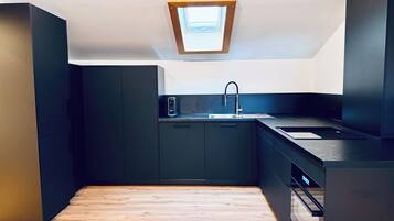 A compact kitchen with dark cabinetry, a modern sink, and a skylight.