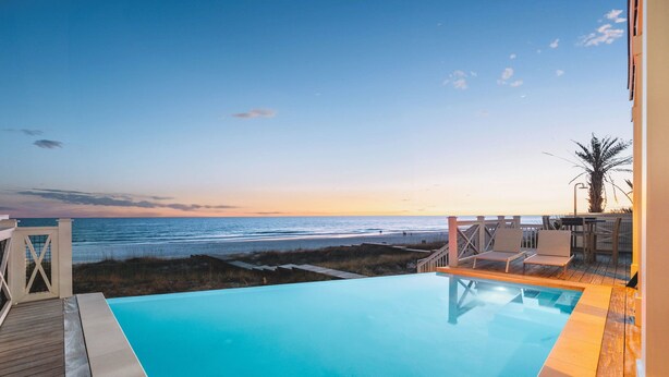 A pool with a view of the beach and ocean at sunset.
