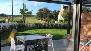 An outdoor patio with a glass enclosure, a table, and chairs. - 1-bedroom gîte with access to covered, heated swimming pool. 2 steps from the sea  (Guissény)