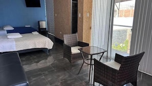 Habitación de hotel con cama, una mesita, dos sillas de mimbre, televisión y vista al exterior.