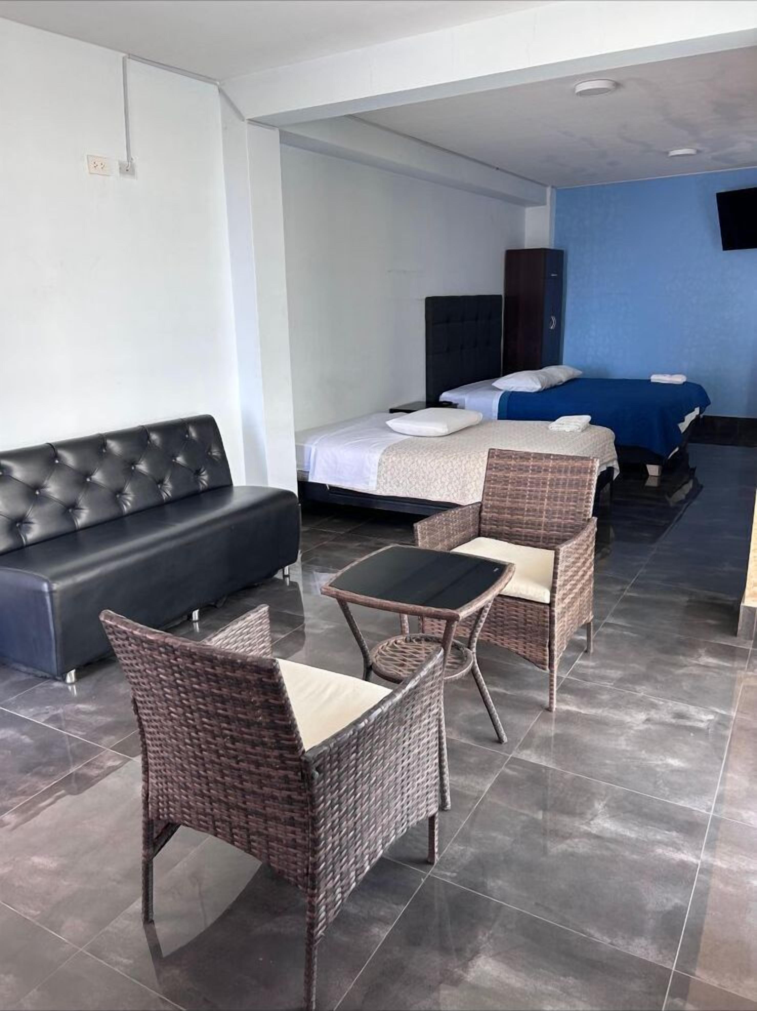 A hotel room with a sofa, two beds, a dining table, and wicker chairs.