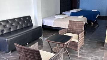 Une chambre d’hôtel avec un canapé, deux lits, une table à manger et des chaises en osier.