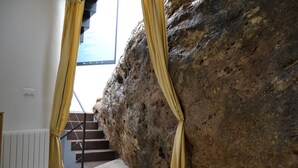 A staircase leading to a balcony with yellow curtains, a rocky wall, and a view of a building. - Villa La Roca - A fusion of modern and typical Andalucian architecture (Montecorto)