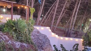 A rocky outdoor area with a pergola and string lights, surrounded by trees and vegetation. - Villa La Roca - A fusion of modern and typical Andalucian architecture (Montecorto)