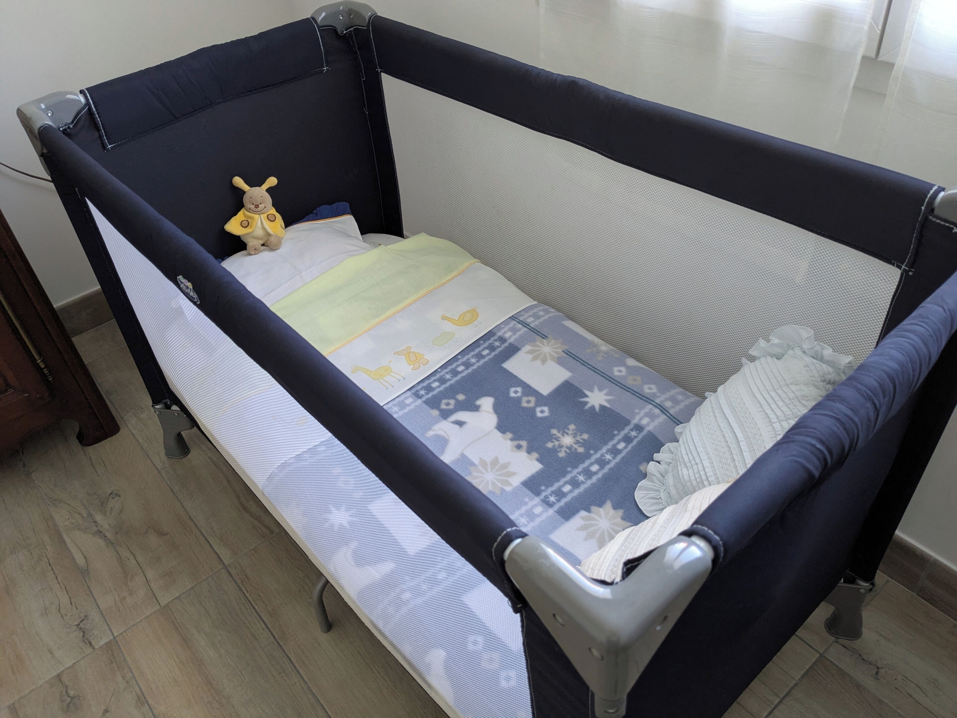 A baby crib with a mesh side, a yellow toy, and a patterned blanket.