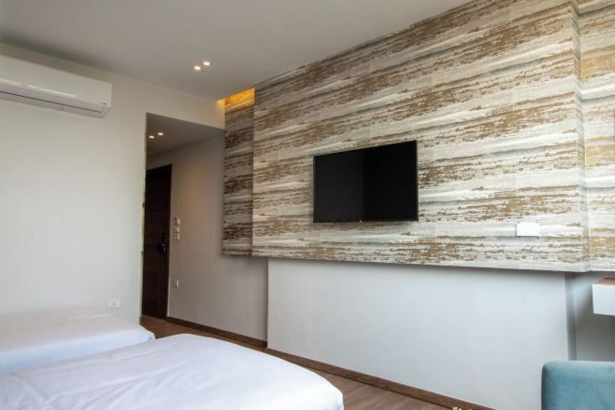A hotel room with a bed, a flat-screen TV mounted on a textured wall, and a small seating area.
