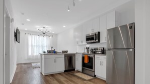 A modern kitchen with white cabinets, stainless steel appliances, and a wooden floor.