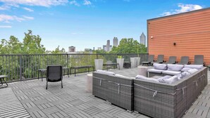 A rooftop deck with outdoor furniture, a view of the city skyline, and a wooden building.