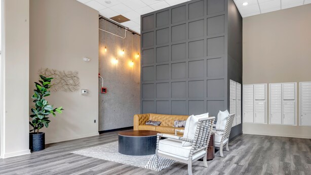 A modern lobby with a leather sofa, a white armchair, a round coffee table, and a potted plant.