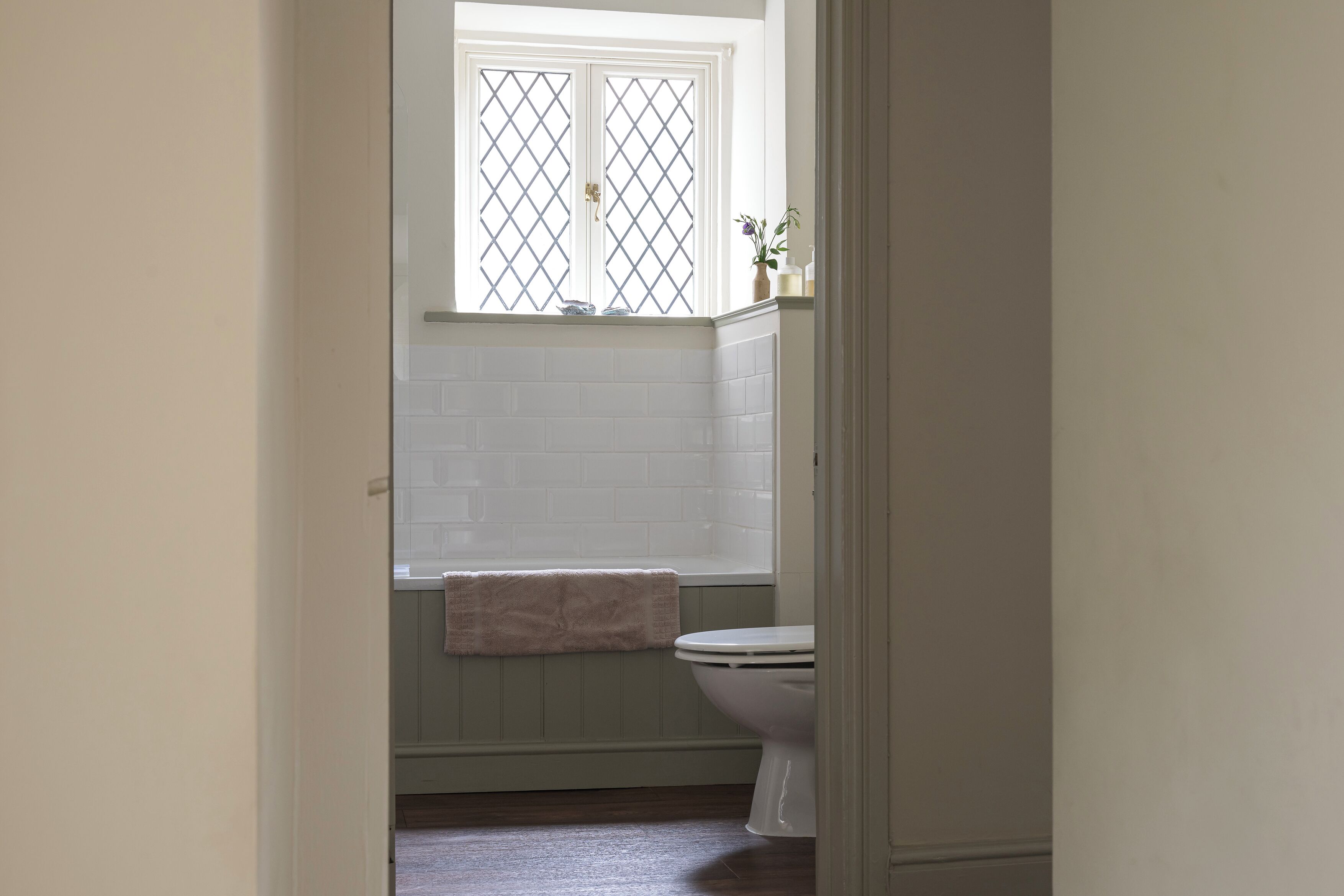 A bathroom with a white toilet, a window with a diamond pattern, and a towel hanging on the wall.