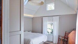 A bedroom with a bed, a window with curtains, a wooden chair, and a ceiling light fixture. - Cottage Duinroos - Dune Rose (Oostvoorne)