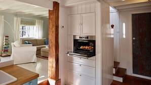 A compact kitchen with a built-in oven, wooden accents, and a view into the living area. - Cottage Duinroos - Dune Rose (Oostvoorne)