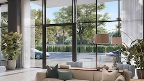 A modern living room with a beige sofa, a coffee table, and a large window offering a view of a street with cars and greenery. - 580 Residance (Miami Beach)