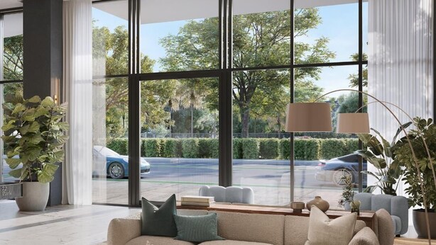 A modern living room with a beige sofa, a coffee table, and a large window offering a view of a street with cars and greenery. - 580 Residance (Miami Beach)