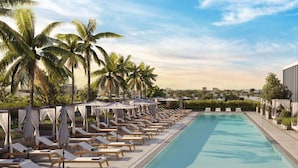 A swimming pool with lounge chairs and umbrellas, surrounded by palm trees, with a view of the cityscape. - 580 Residance (Miami Beach)