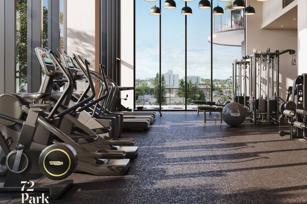 A gym with treadmills, weights, and exercise balls, large windows, and pendant lighting.