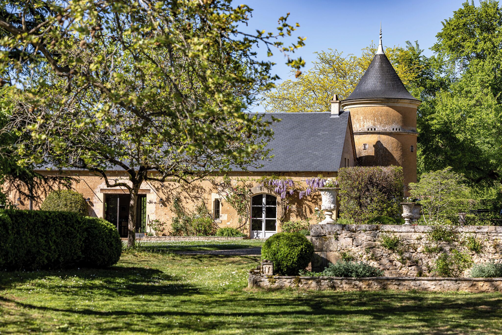 A historic building with a tower, a well-maintained lawn, and a stone wall.