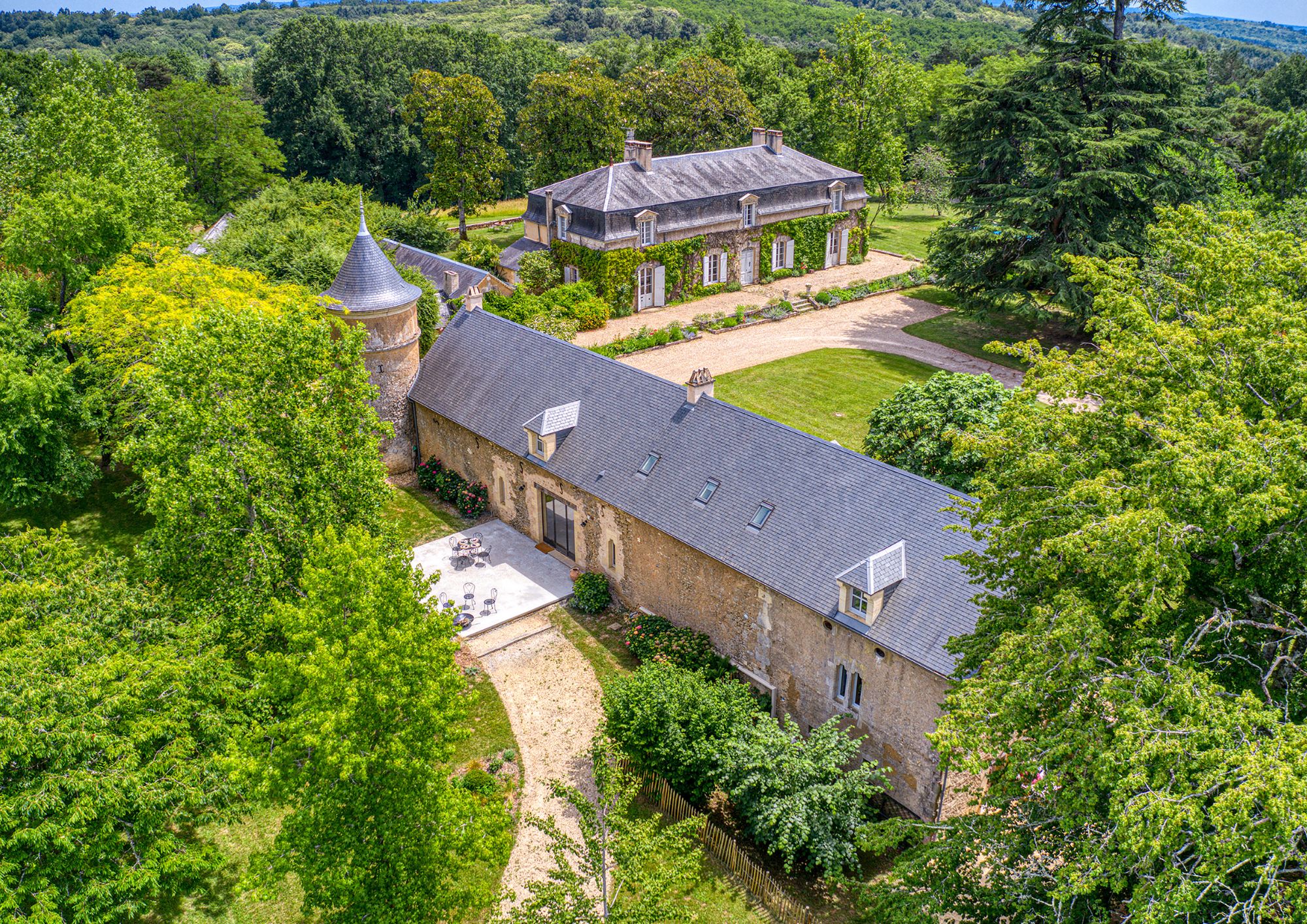 A large stone building with a tiled roof, surrounded by lush greenery and a well-maintained lawn.