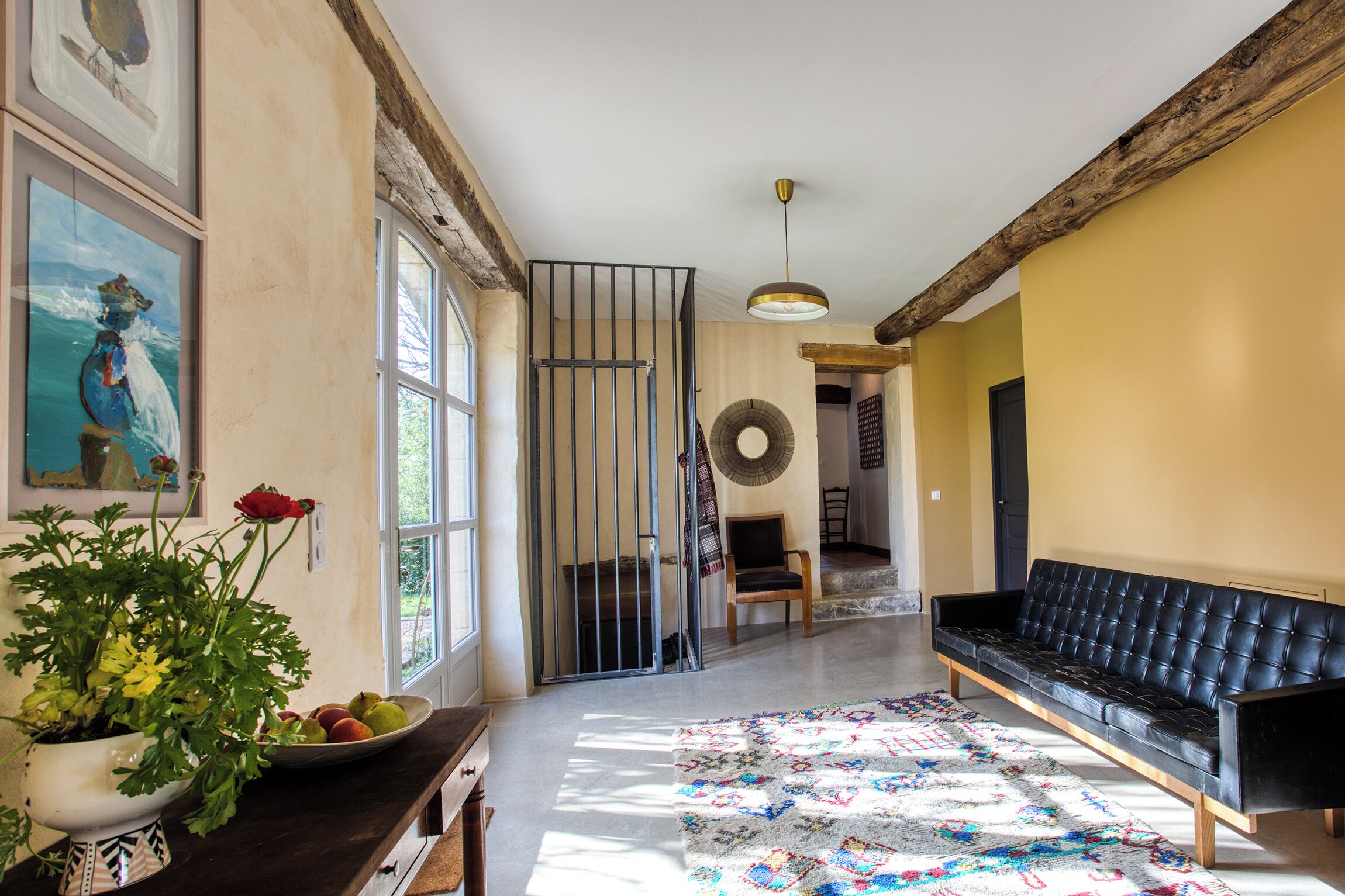 A living room with a sofa, a rug, a plant, and a painting on the wall.