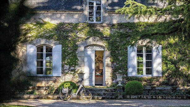 A stone building with a central door, two windows with shutters, and a bicycle parked in front.
