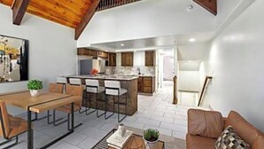 Una cocina moderna con una isla central, vigas de techo de madera y un comedor con mesa y sillas.