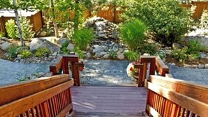 Una terraza de madera que lleva a un jardín con una cascada pequeña y rocas.