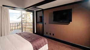 A hotel room with a large bed, a television mounted on the wall, and a balcony with a view of the outdoors.