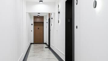 A modern hallway with white walls, black and white marble flooring, recessed lighting, and a wooden door at the end.