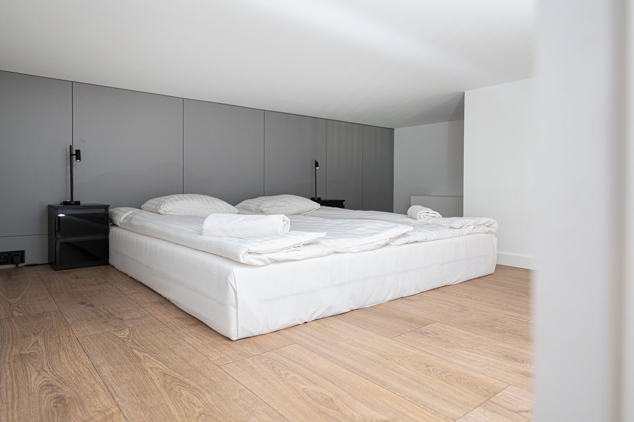 A modern bedroom with a large bed, a nightstand, and a bedside table.