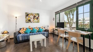 Un saló modern amb un sofà, una taula de dinar i cadires. Hi ha un quadre a la paret, una làmpada i una finestra amb vistes als arbres.