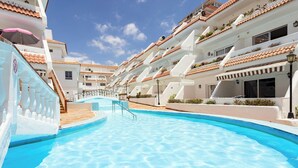 Une piscine à l’eau d’un bleu limpide, entourée de bâtiments blancs aux toits recouverts de tuiles rouges et dotés de balcons.