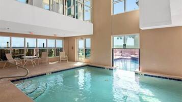 An indoor swimming pool with clear blue water, surrounded by large windows offering views of the outside.