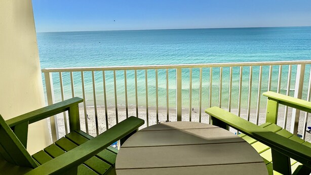 A balcony with a view of the ocean, featuring a wooden deck and two green chairs.