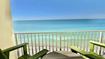 A balcony with a view of the ocean, featuring a wooden deck and two green chairs.